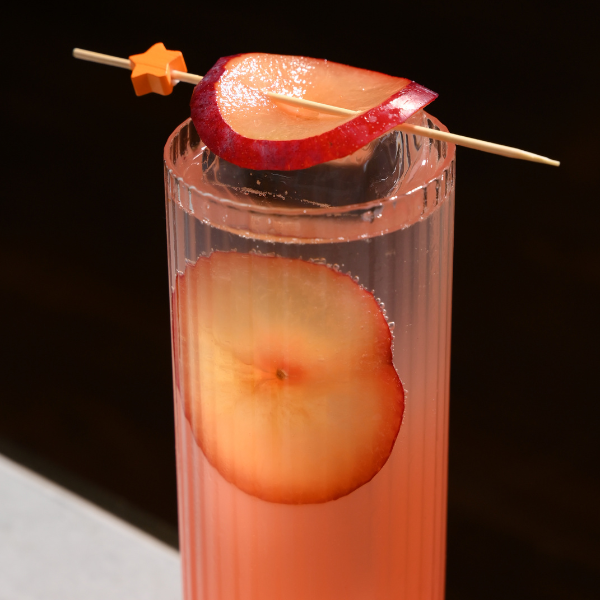 Fresh fruit drink served in a tall glass, garnished with a sliced red apple and decorative cocktail skewer.