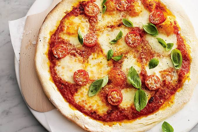 Freshly baked Corner Cafe pizza topped with melted mozzarella cheese, tomato sauce, fresh basil leaves, and herbs on a wooden serving board.