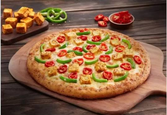Corner Cafe pizza topped with paneer cubes, green bell peppers, sliced red chilies, and melted cheese on a wooden serving board.