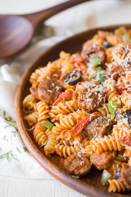Delicious spiral pasta served with savory meat, colorful vegetables, tomato sauce, and grated cheese in a wooden bowl.