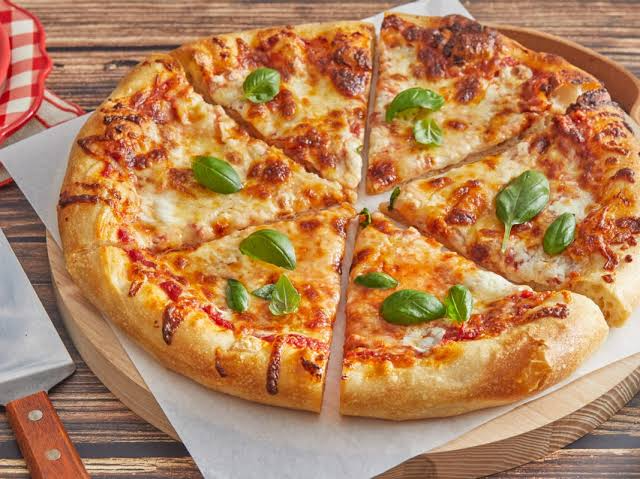 Freshly baked cheese pizza sliced into pieces, topped with tomato sauce, melted mozzarella cheese, and fresh basil leaves on a wooden serving board.