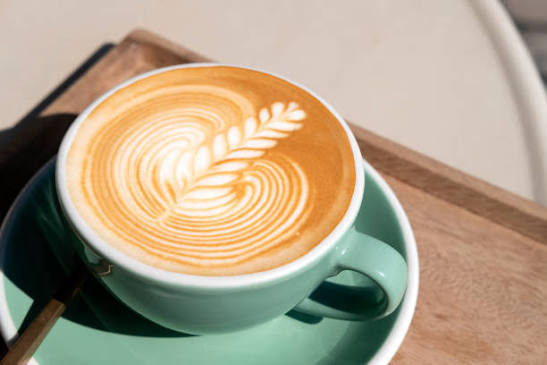 Corner Cafe latte featuring beautiful heart-shaped latte art served in a green ceramic cup and saucer on a wooden tray.