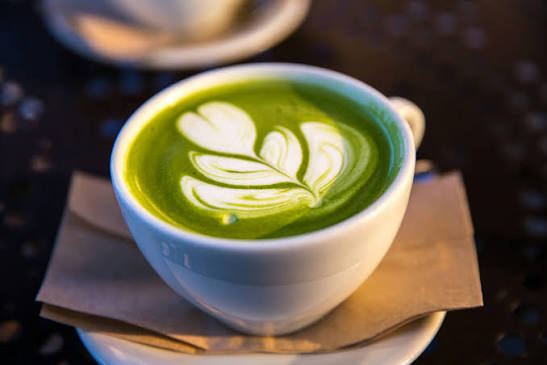 Corner Cafe matcha latte served in a white cup with beautiful leaf-shaped foam art on a saucer.