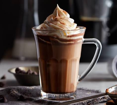 Corner Cafe creamy chocolate coffee topped with whipped cream and chocolate drizzle, served in a clear glass mug.
